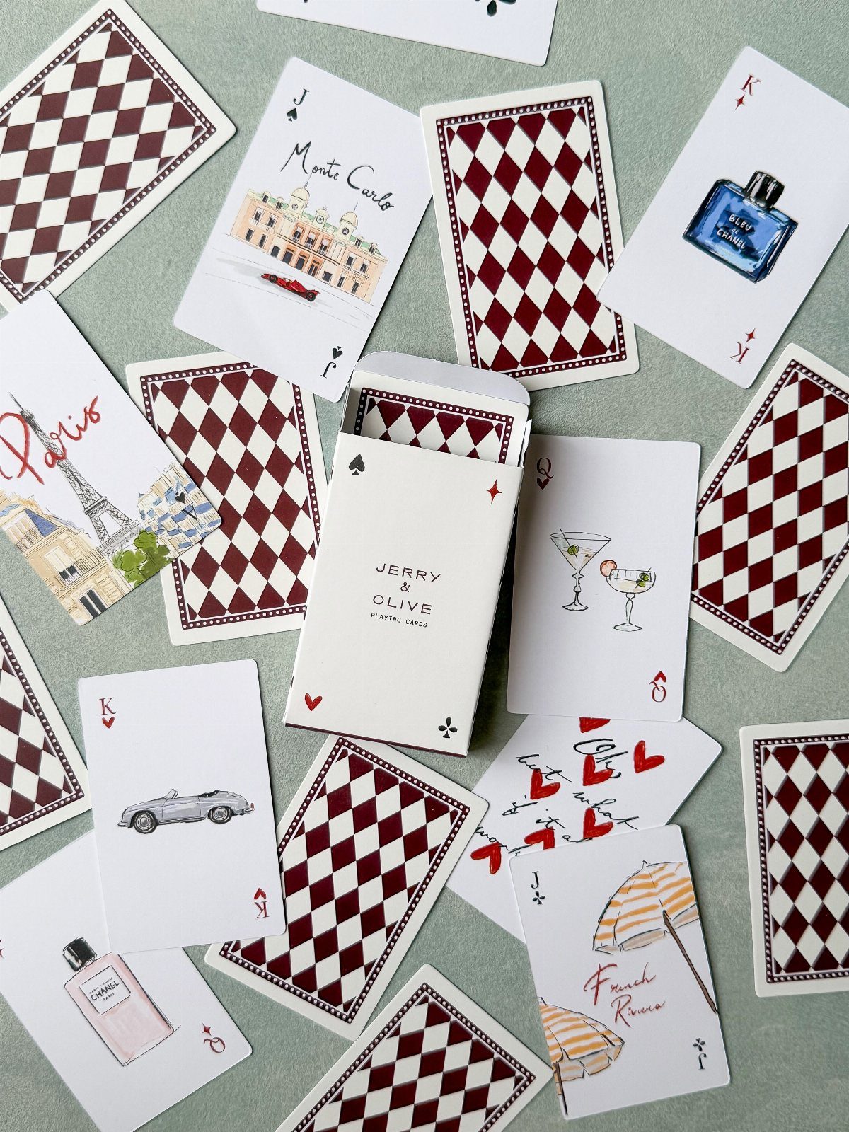 Custom playing cards with red diamond backs and travel illustrations scattered around a box.