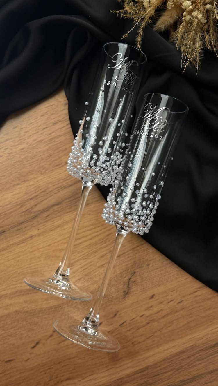 Two engraved champagne flutes decorated with white pearls on a wooden surface.