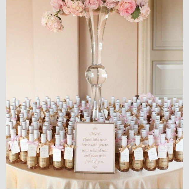 Mini champagne bottles with pink ribbons and a floral centerpiece on a table