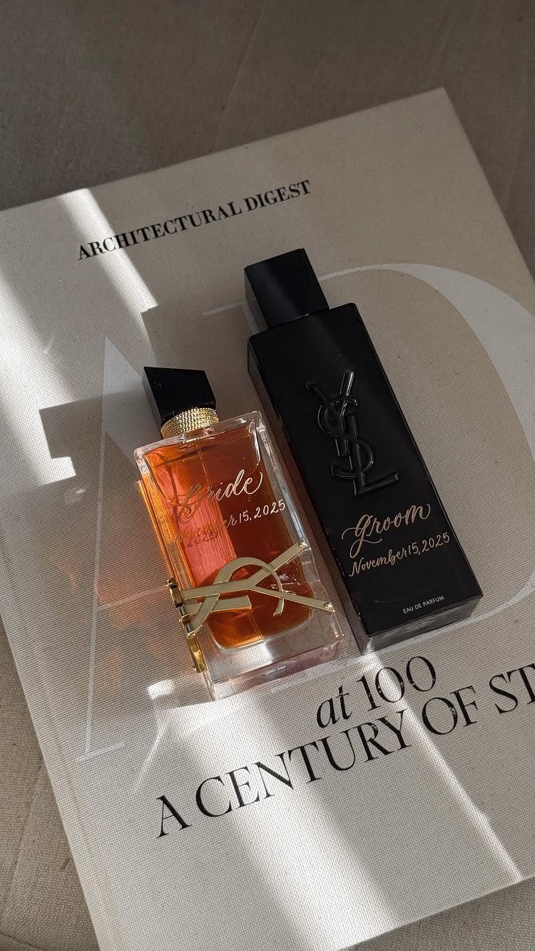 Two personalized perfume bottles with gold calligraphy resting on a white magazine.