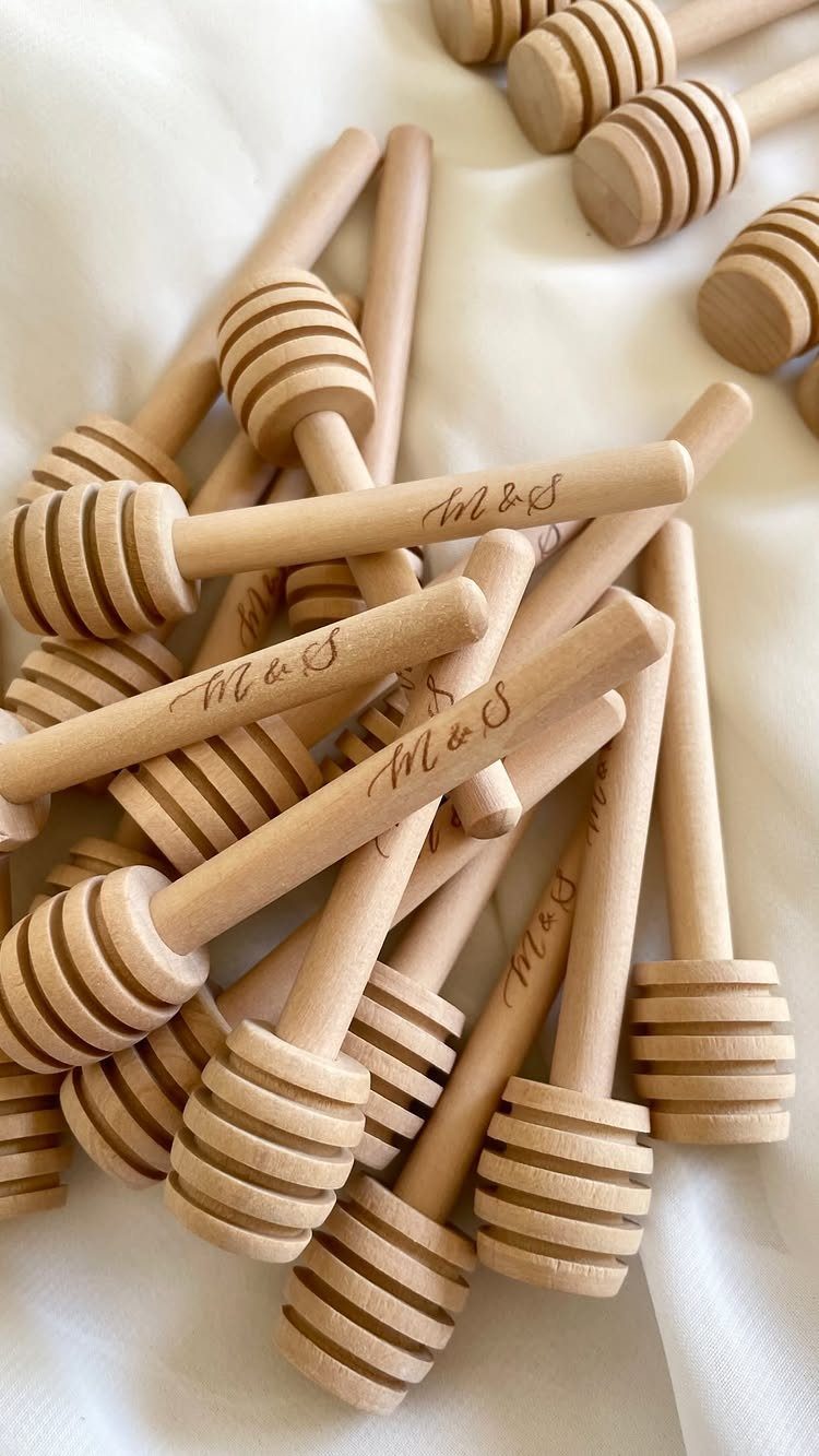 Wooden honey dippers with engraved initials resting on a white fabric background.