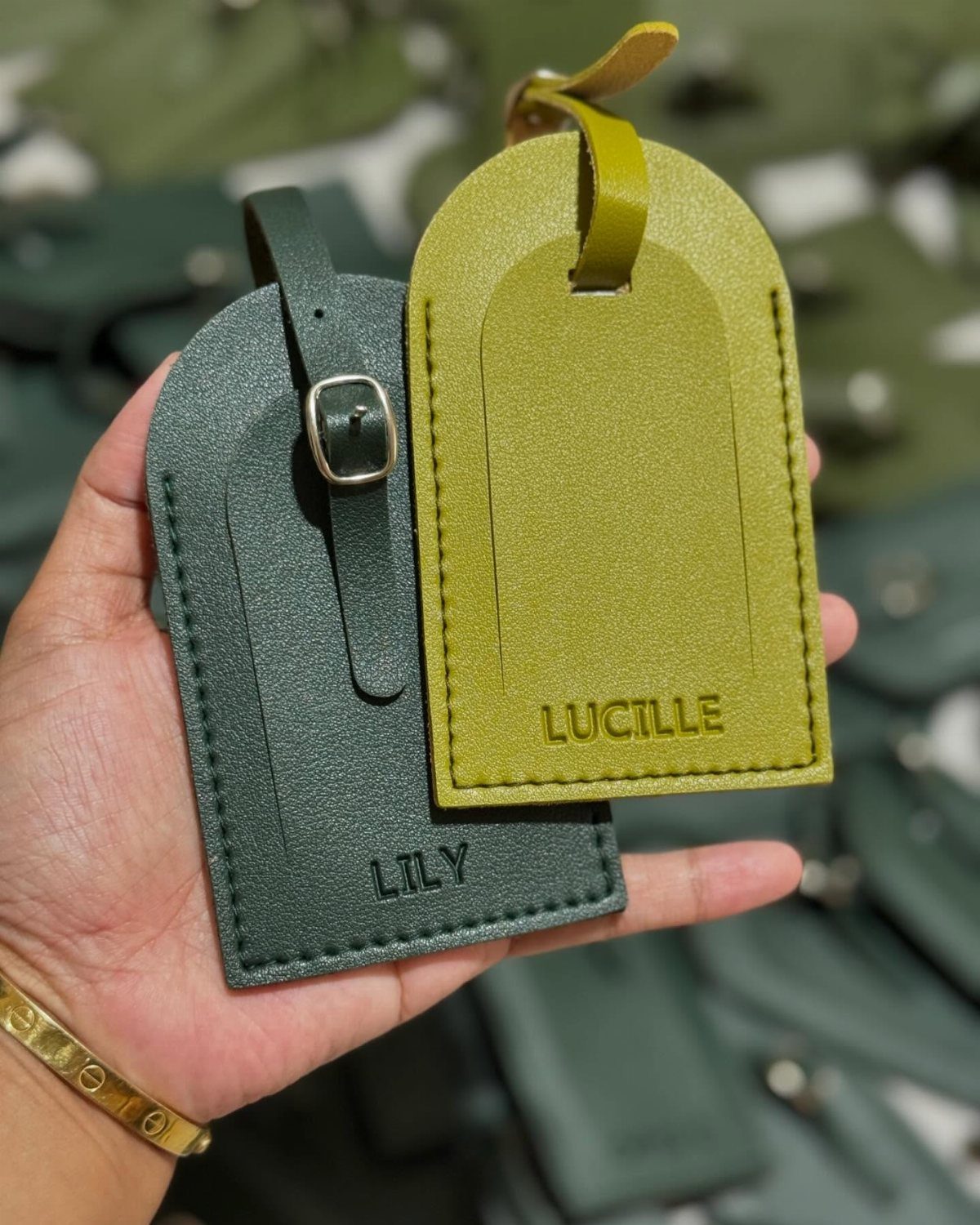 Two leather luggage tags in green tones embossed with personalized names held by hand.