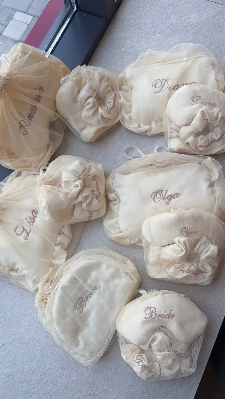 Cream satin sleep masks with embroidered names and the word Bride in cursive script.