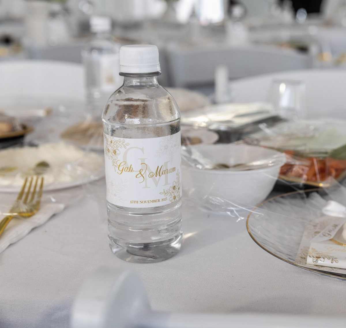 Personalized water bottle with custom wedding label on a white reception table setting.