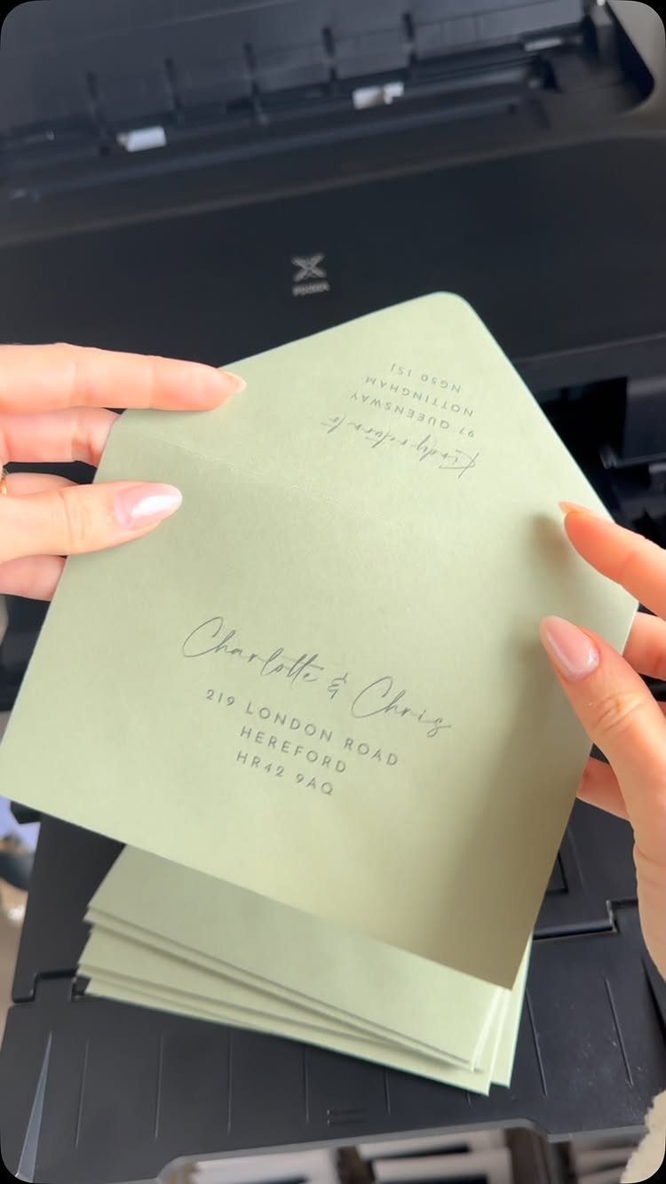 Light green envelopes with printed guest addresses held over a black printer.