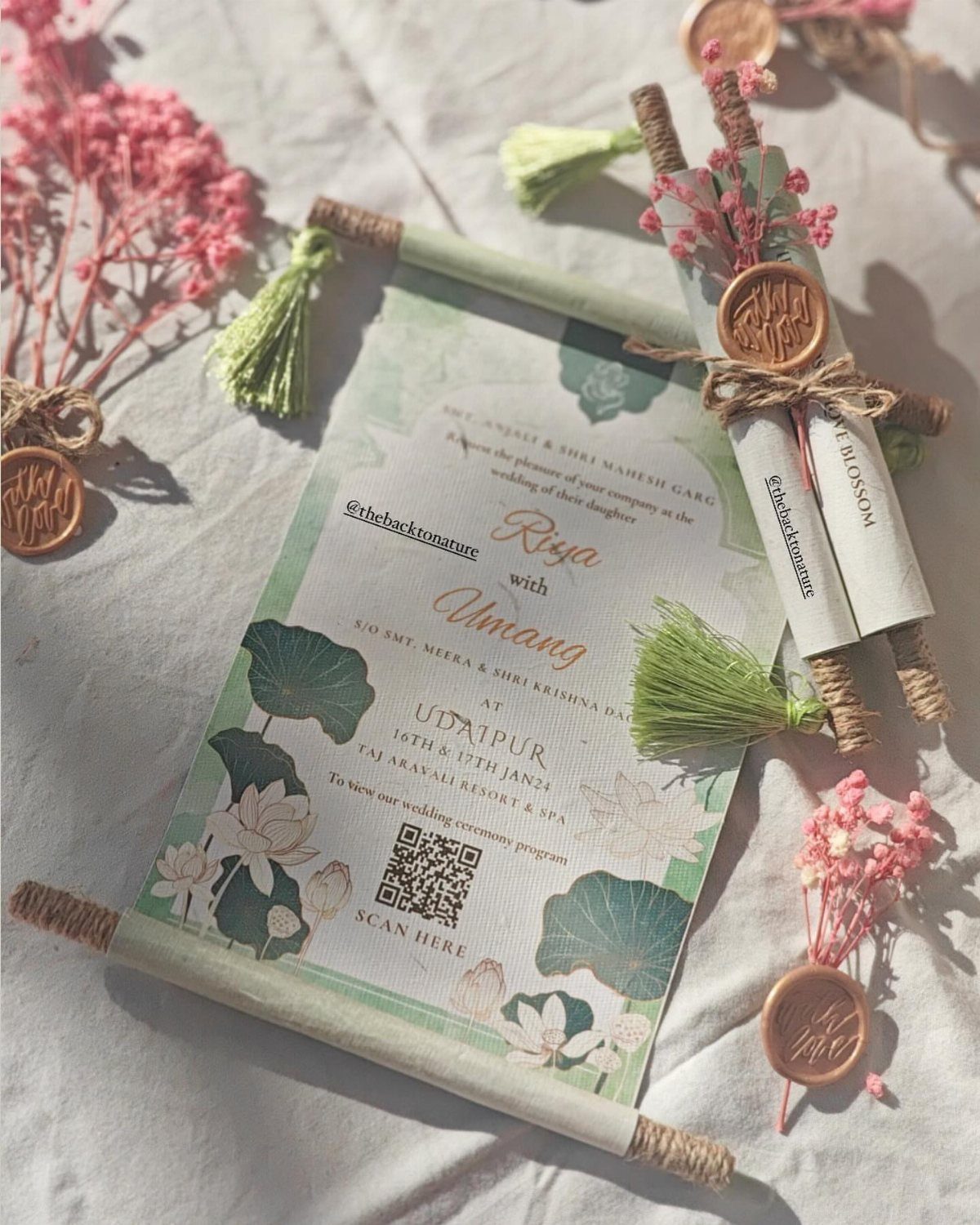 Green scroll wedding invitation with floral designs, wax seals, and pink flowers.