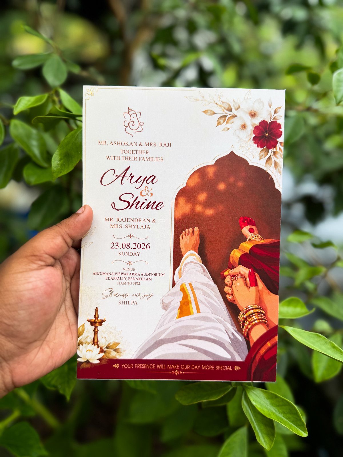 Wedding invitation card with traditional Indian couple illustration held against green foliage.