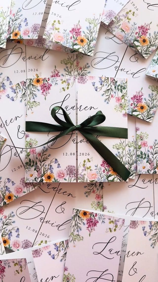 Wedding invitations with colorful watercolor wildflowers tied with a dark green satin ribbon.