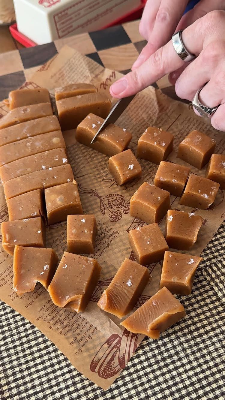 Brown salted caramel squares being cut on parchment paper over a checkered cloth.
