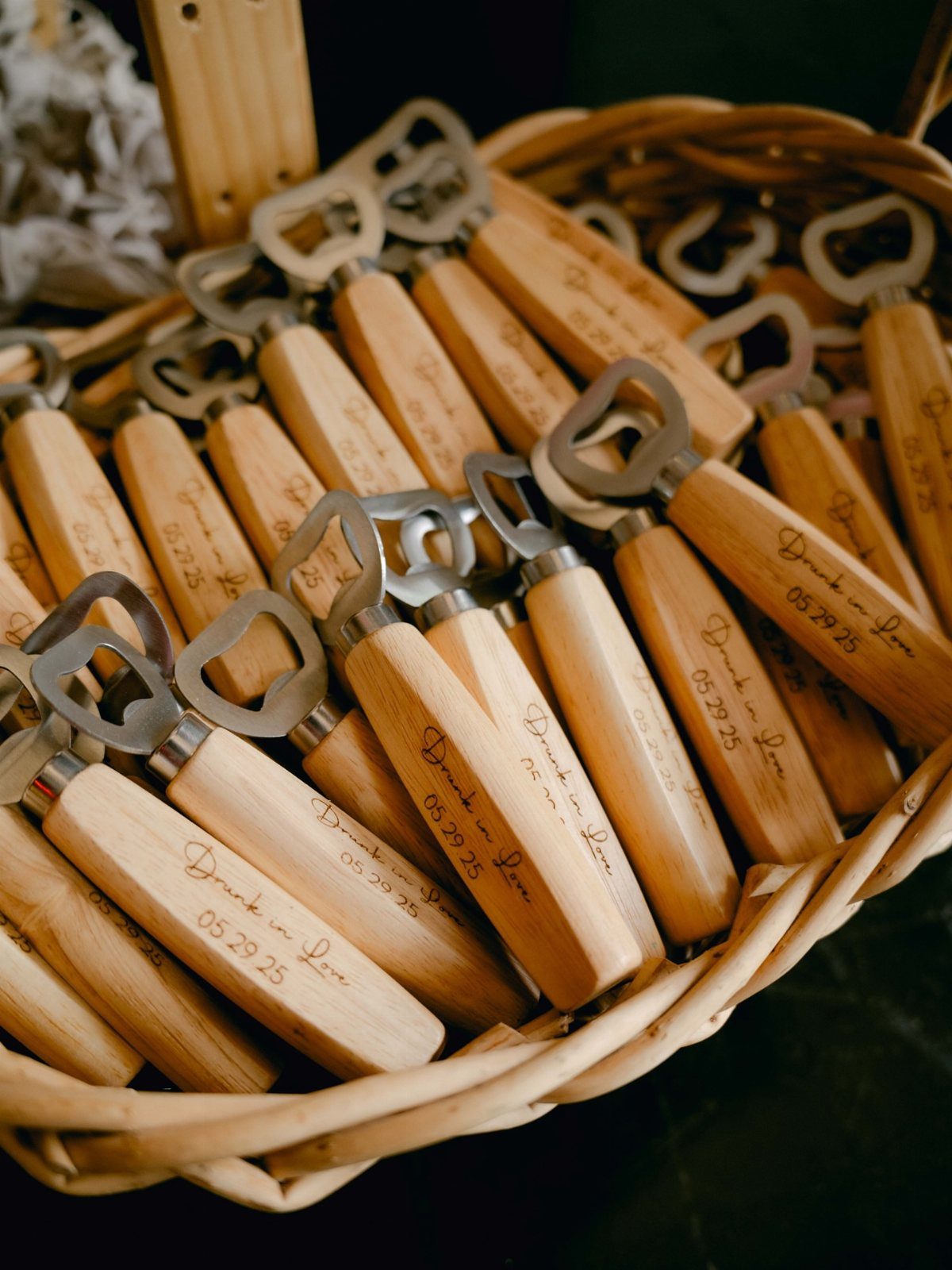 Personalized wooden bottle openers with engraved dates resting in a woven wicker basket.