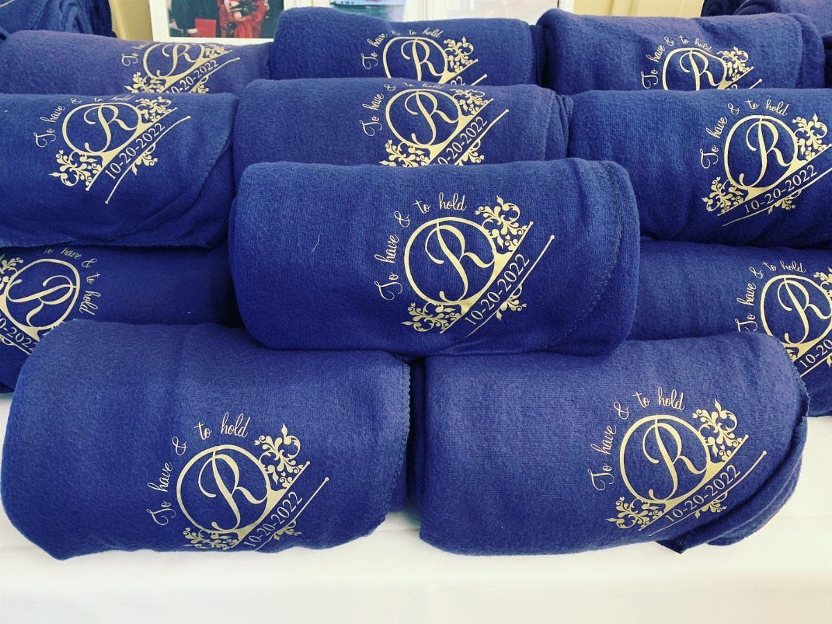 Folded royal blue fleece blankets with gold foil wedding monograms and dates.