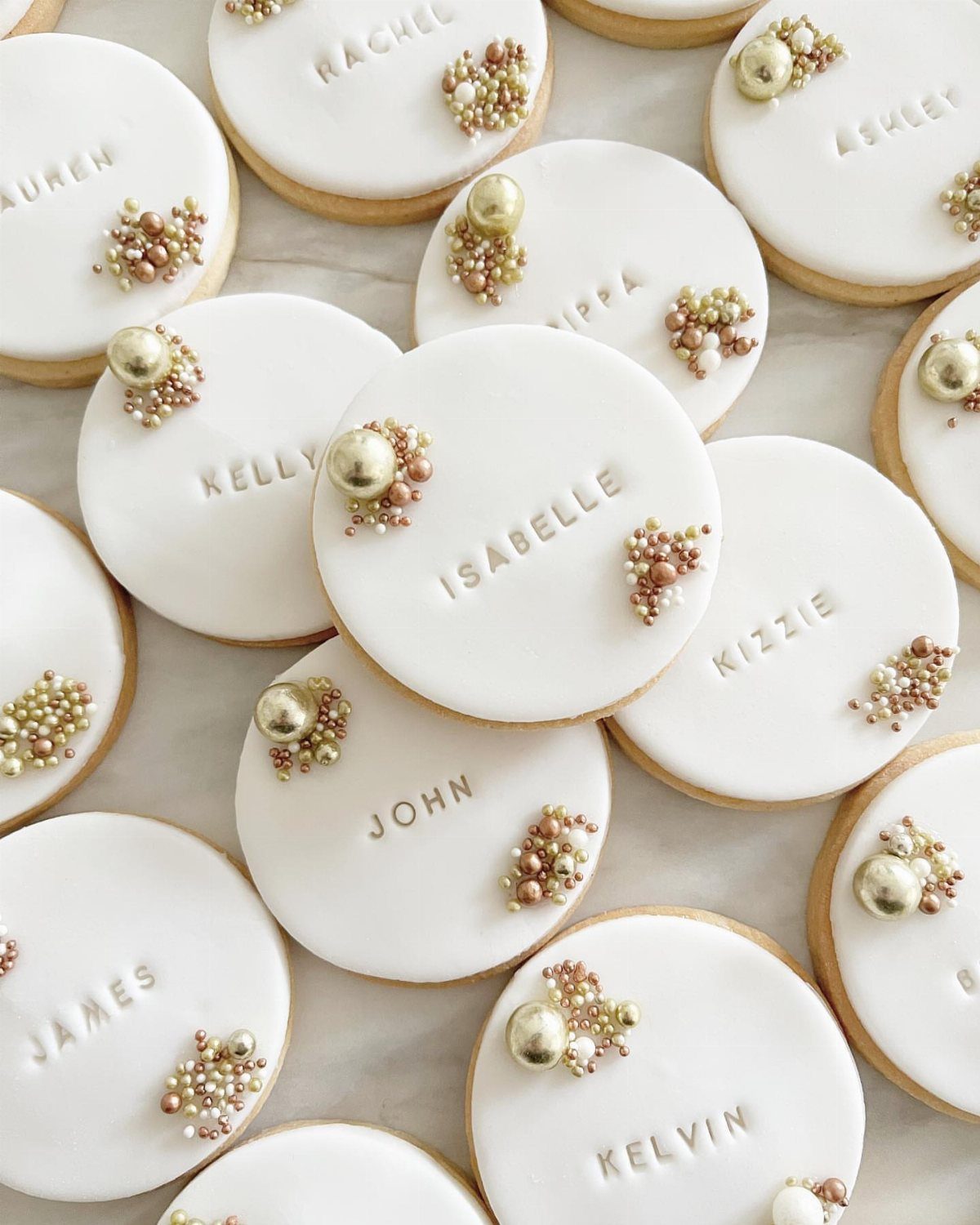 Round white fondant cookies with embossed names and gold pearl sprinkles for guests.