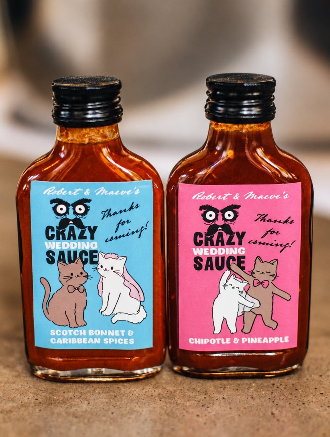 Two mini hot sauce bottles with custom wedding labels featuring cute cartoon cats.