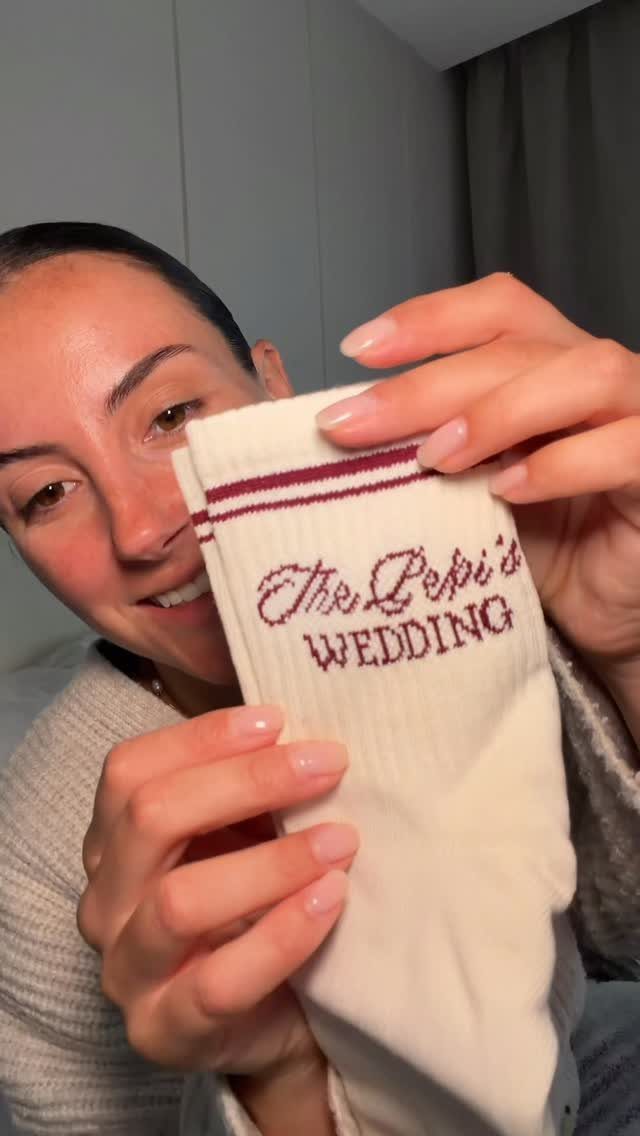 Woman holding a white wedding favor sock with red embroidered wedding text.