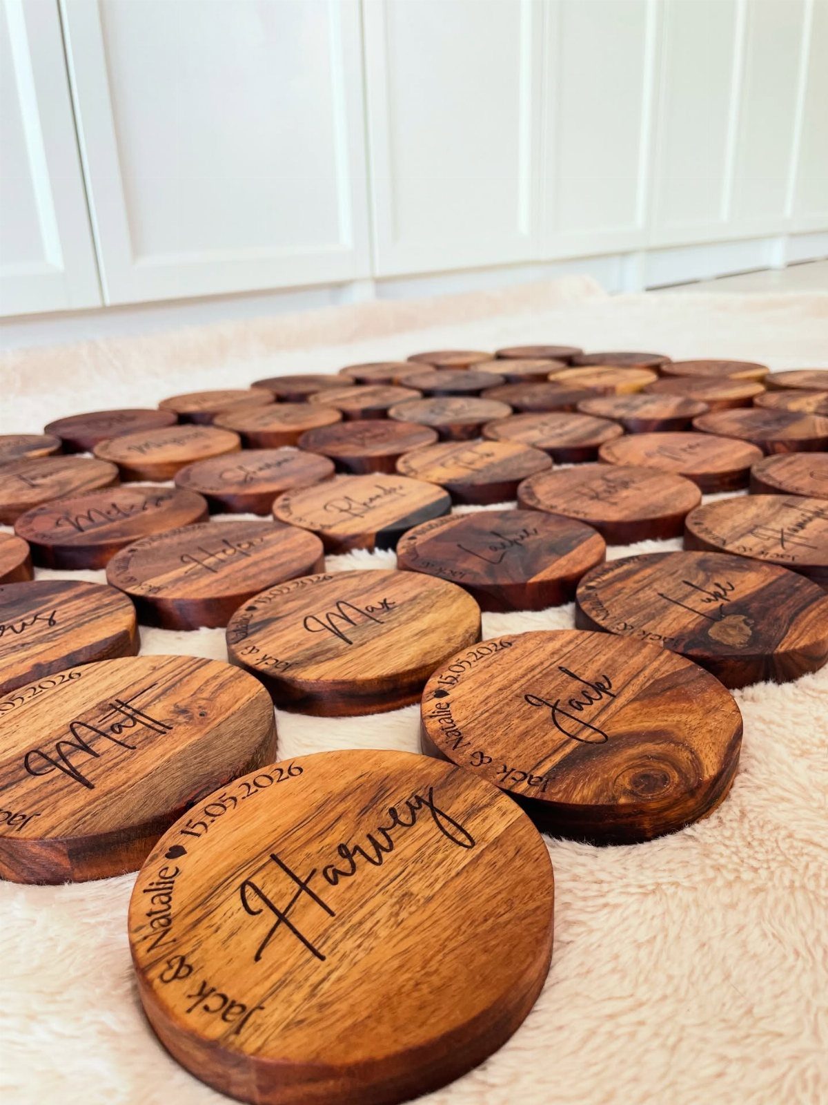 Circular wooden coasters with engraved names and dates arranged on a white rug.