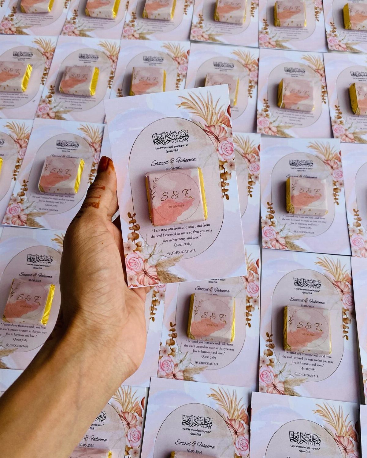 Wedding invitation card with a small pink chocolate bar attached and floral designs.
