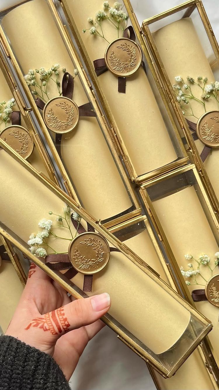 Rolled beige parchment invitation in a gold glass box with wax seal and flowers