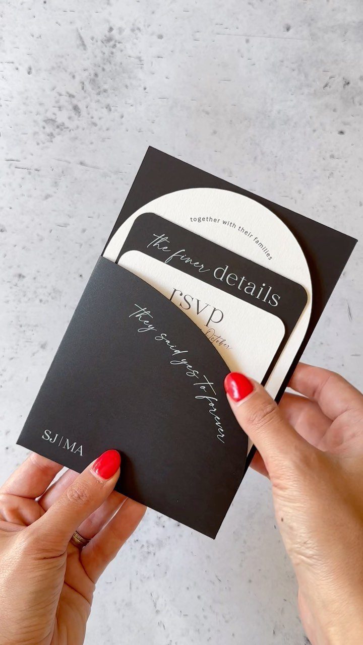 Black and white wedding invitation suite with cursive text held by two hands.