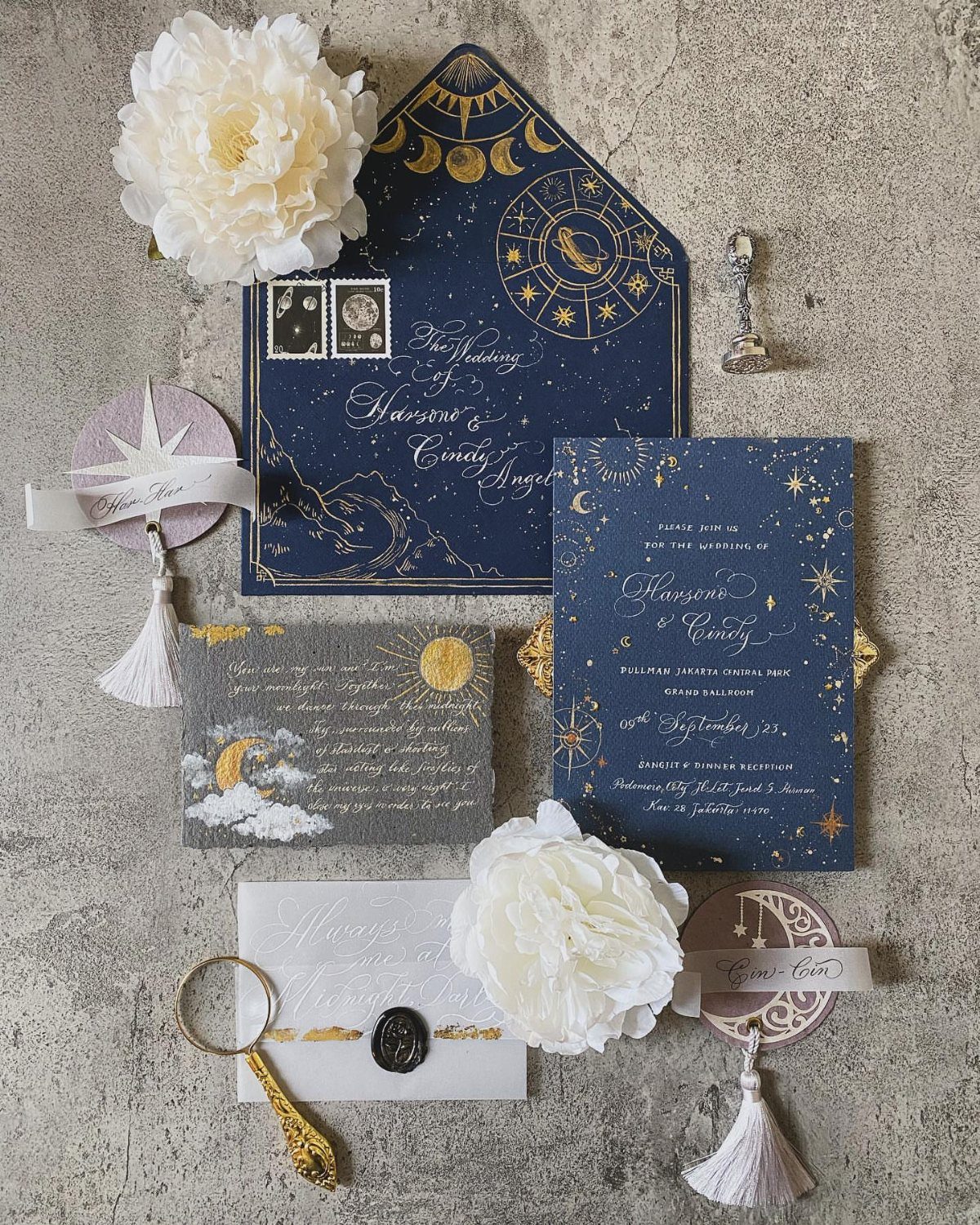 Navy blue wedding stationery with gold celestial motifs, stars, and white peonies.