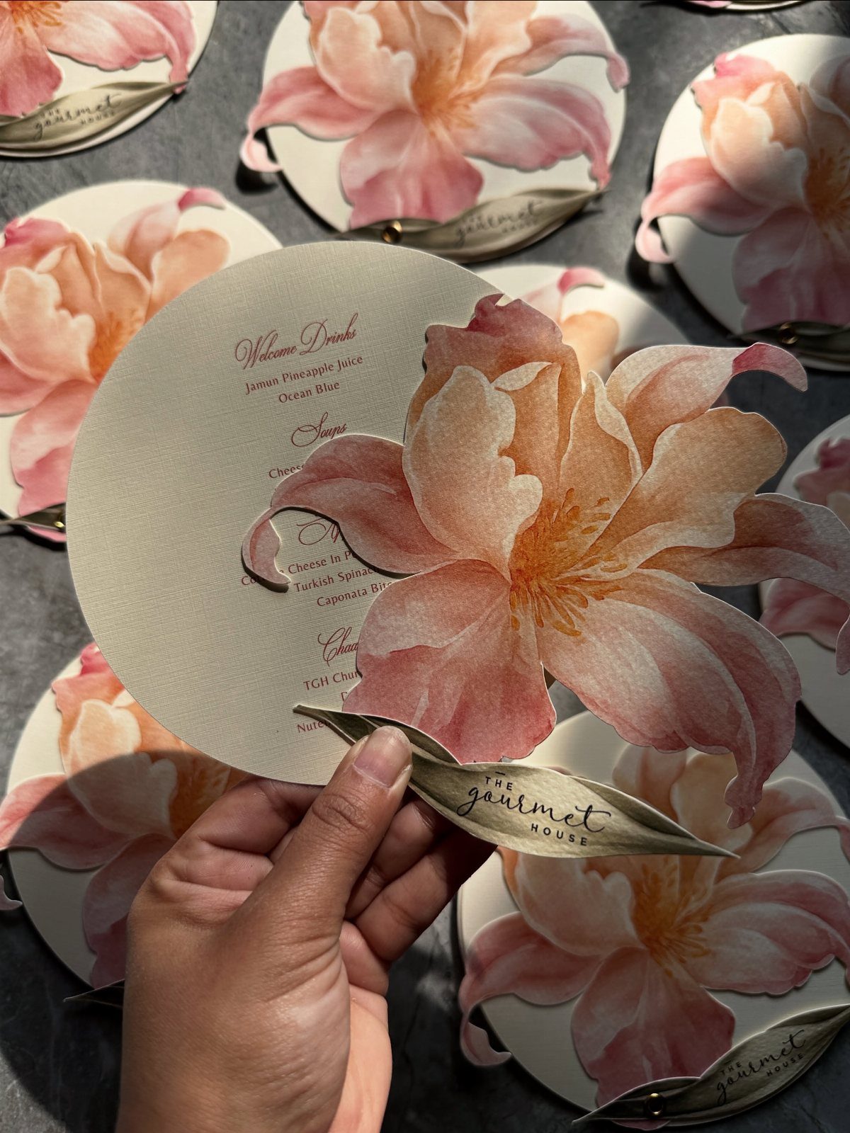 Circular cream invitation with a large 3D pink floral cutout held by hand.