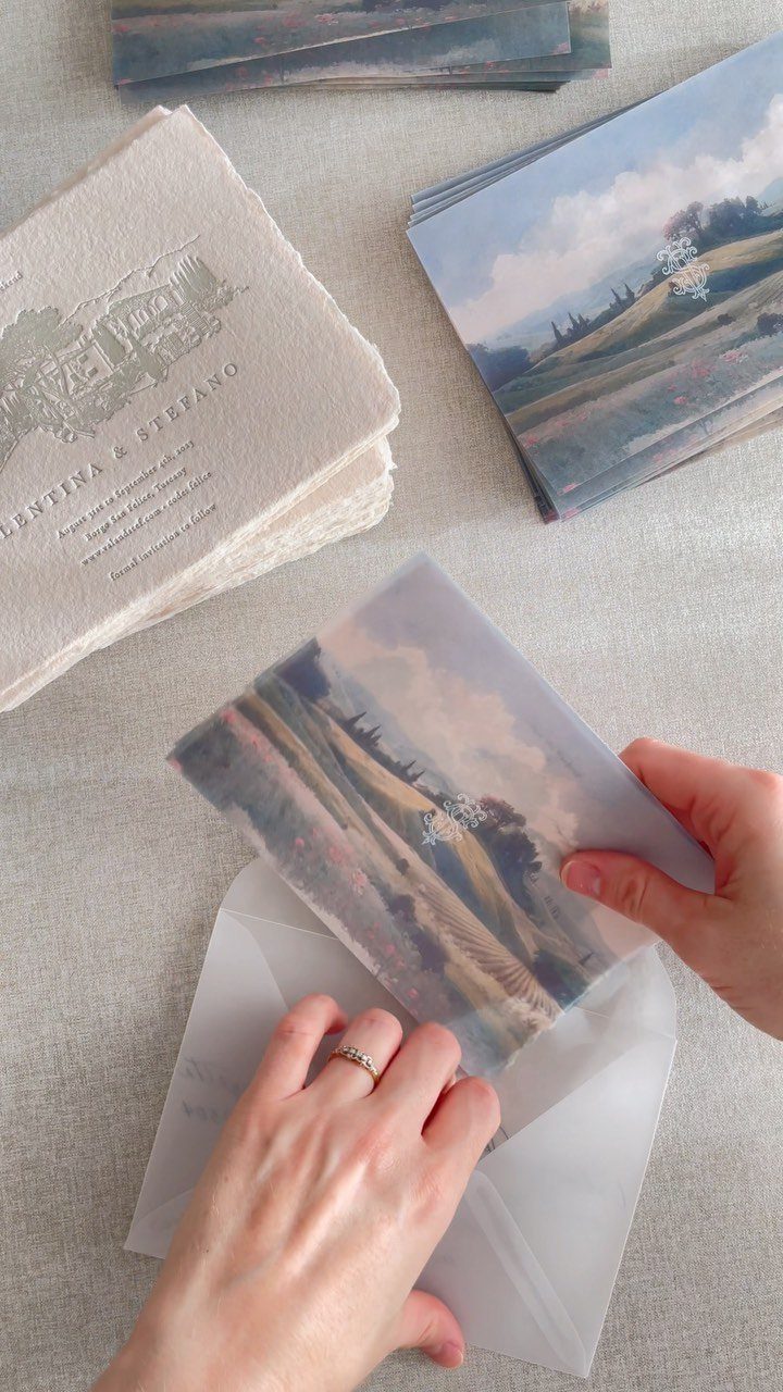 Hands placing an illustrated wedding invitation into a translucent vellum envelope.
