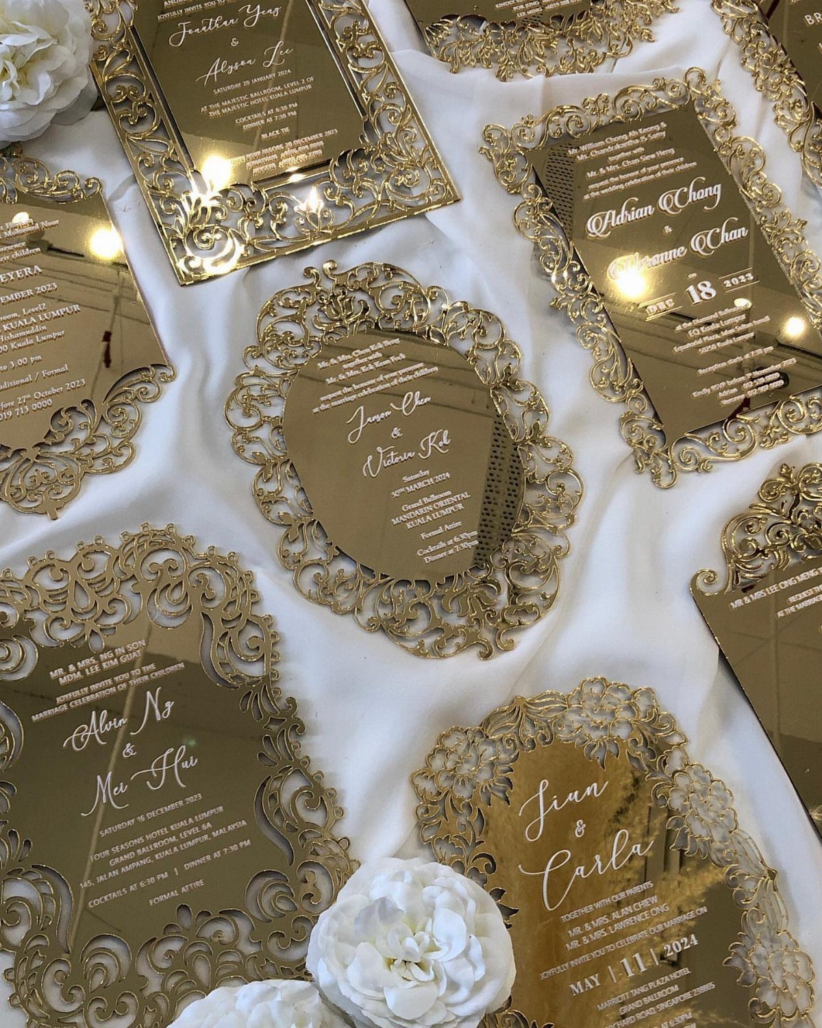 Gold acrylic wedding invitations with intricate laser-cut lace borders on white fabric.