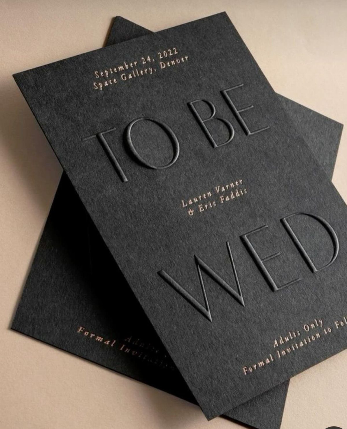 Black textured wedding invitations with embossed lettering and gold foil accents.