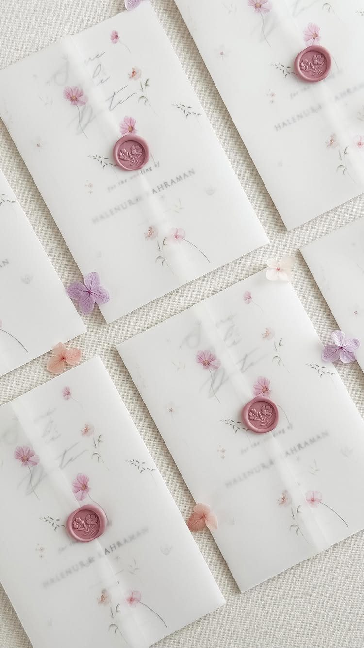 White wedding invitations featuring pink floral patterns and purple wax seals with petals.