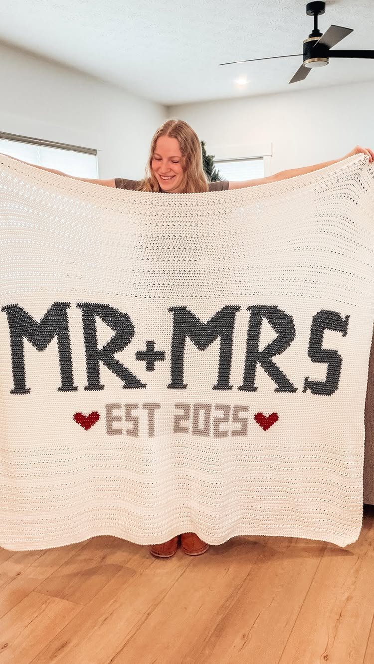 Woman holding a white crochet blanket with Mr and Mrs text and red hearts.