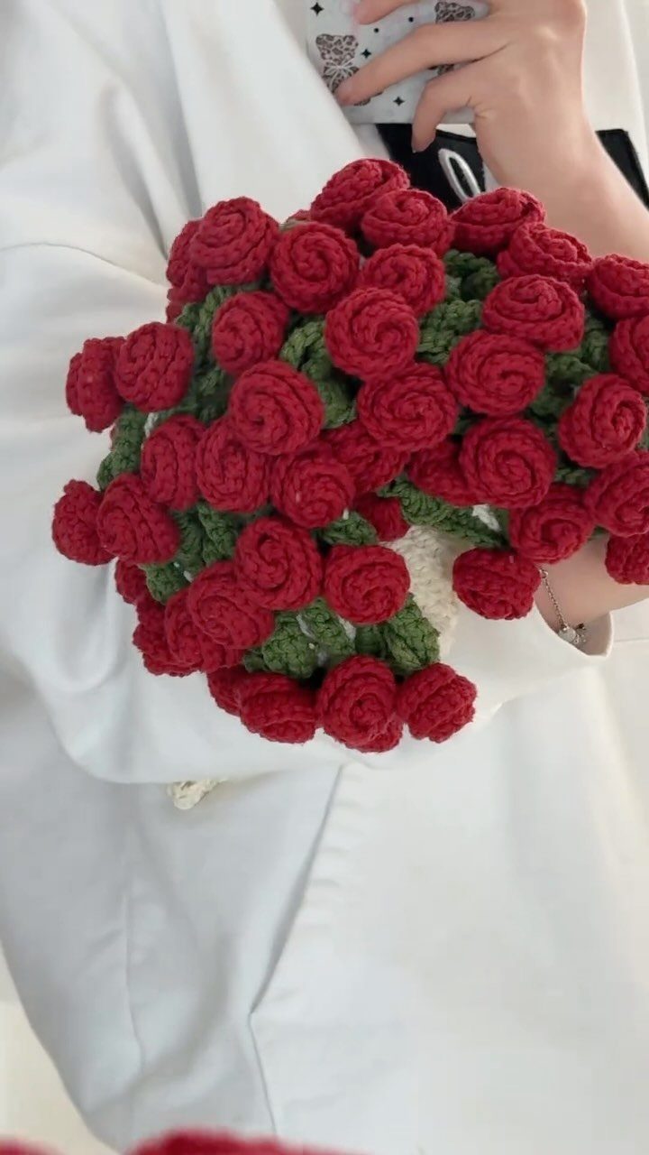 Bouquet of red crochet roses held by a person in white clothing.