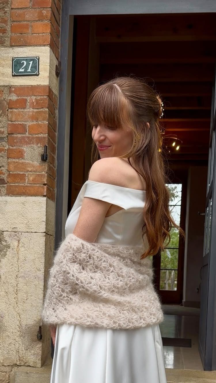 Woman in a white dress wearing a fluffy cream crochet wedding shawl.