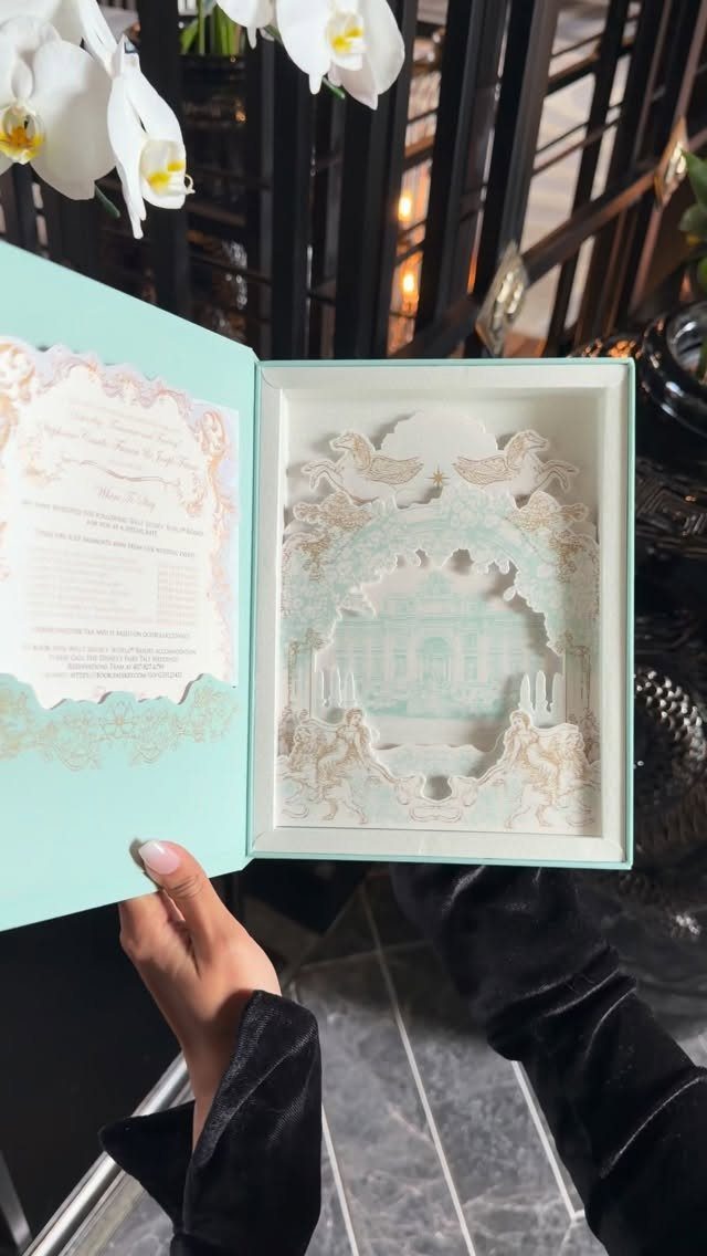 Laser-cut castle silhouette inside a light blue wedding invitation box held by a person
