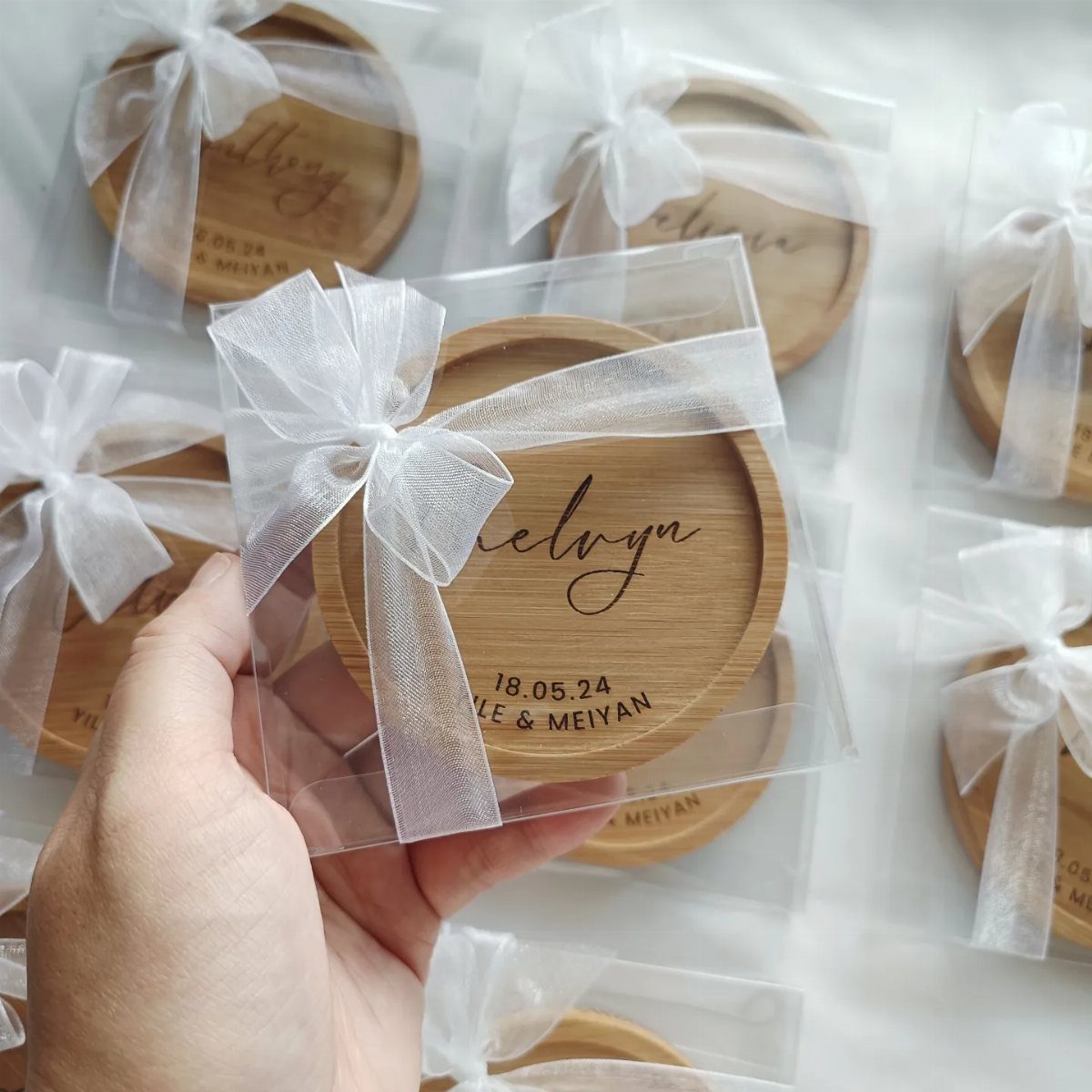 Engraved wooden coasters wrapped in clear plastic with white ribbons for wedding gifts.