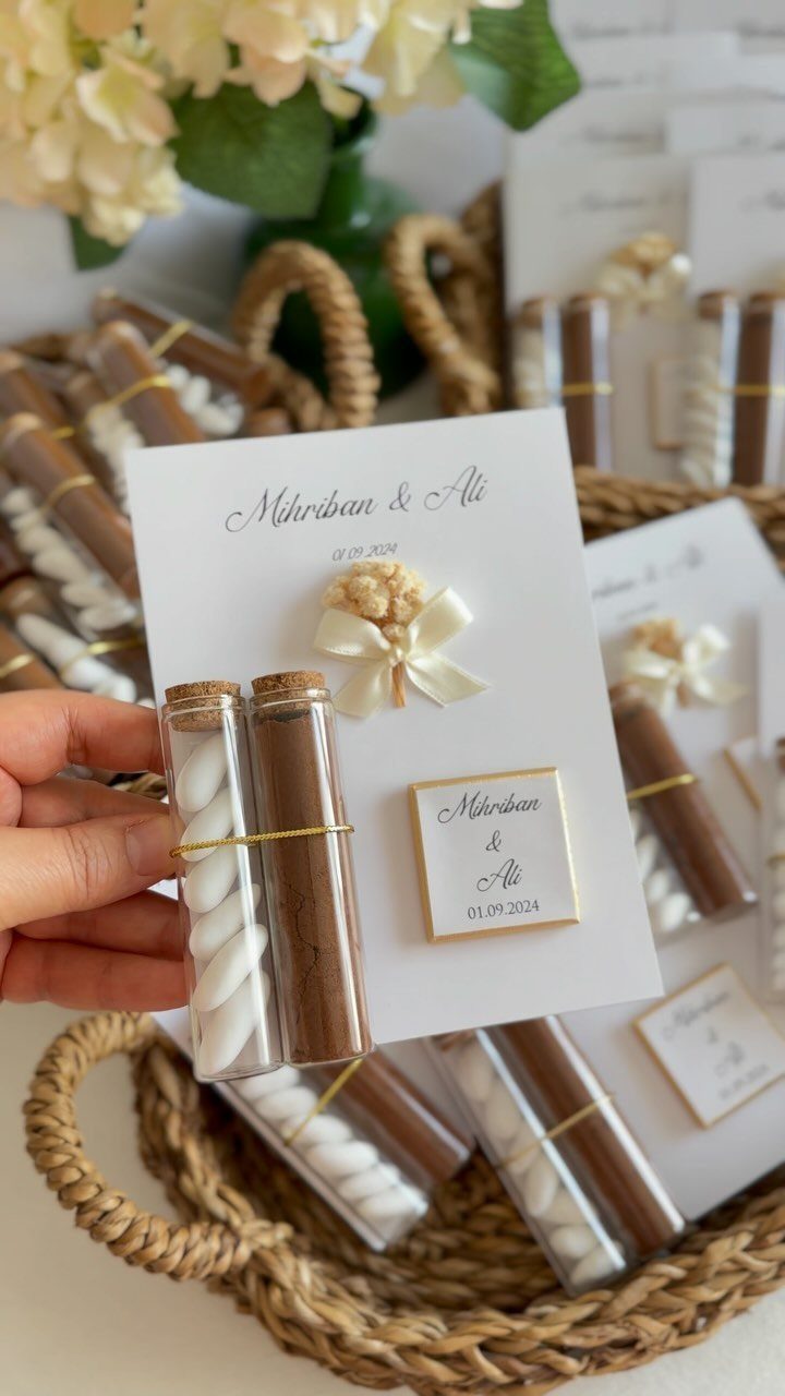 Hand holding a wedding favor card with cocoa and marshmallow vials in glass tubes.