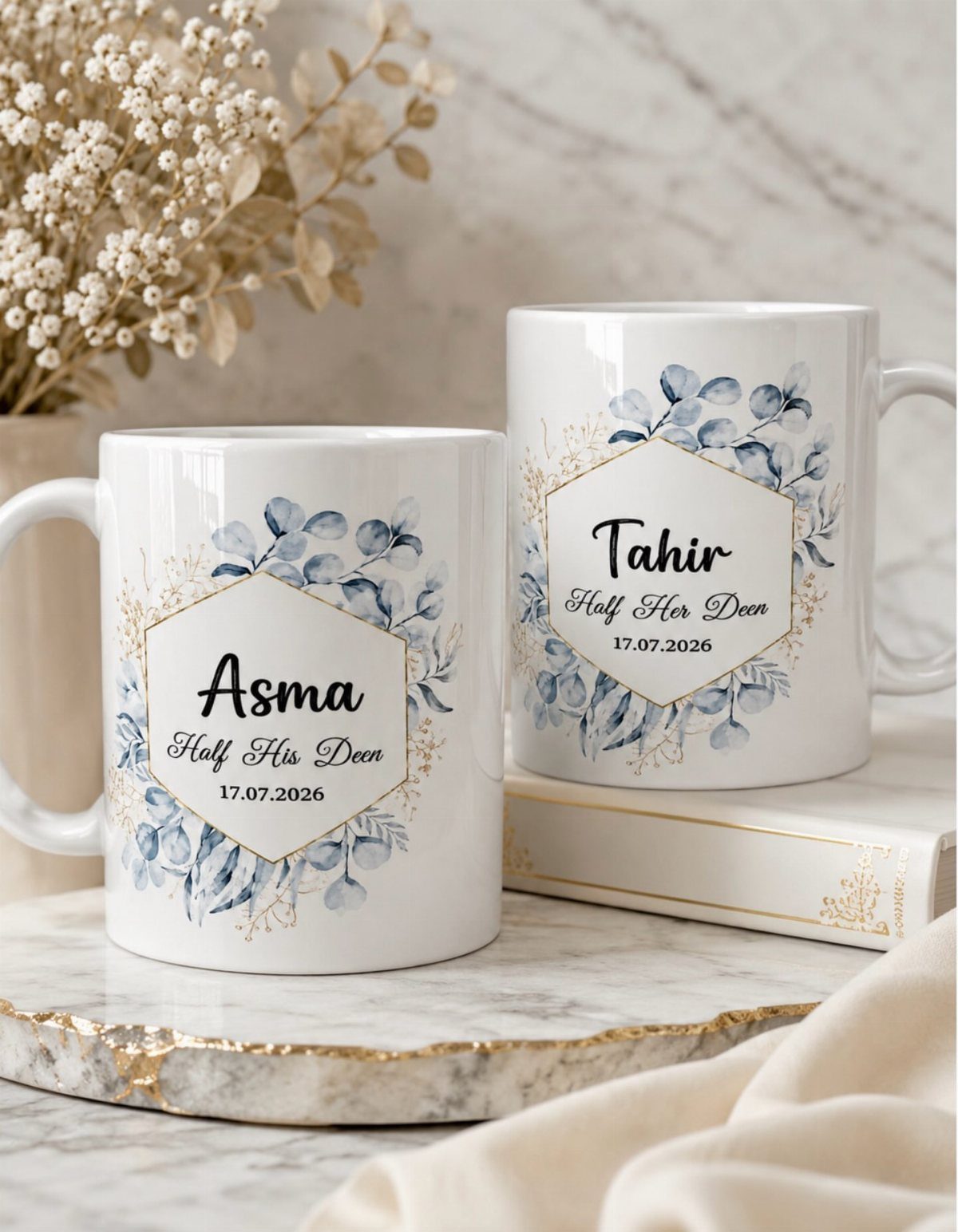 Two personalized white mugs with blue floral patterns and names on a marble surface.