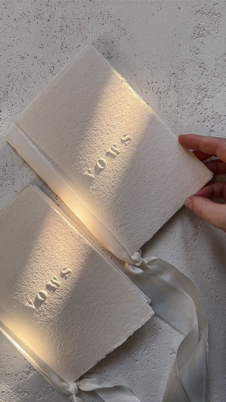 Two white textured vow books with embossed text and white satin ribbon ties.