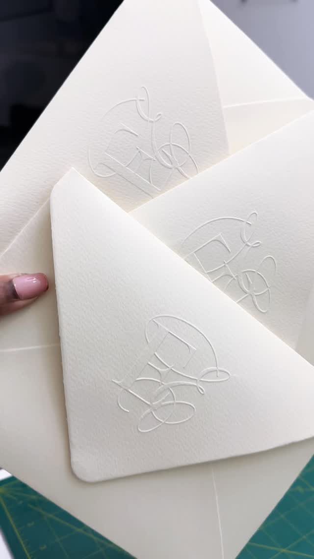 White textured envelopes and cards with blind embossed monograms held by a hand.