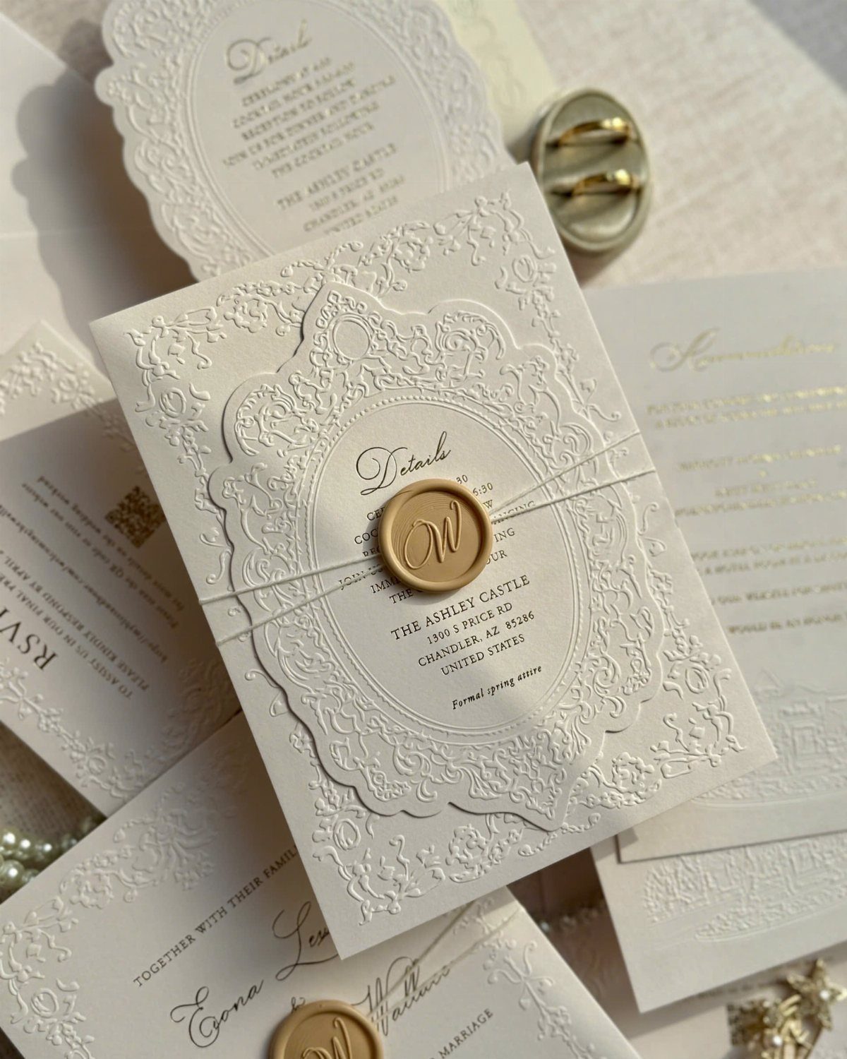 White embossed wedding invitations with floral patterns and a gold wax seal.
