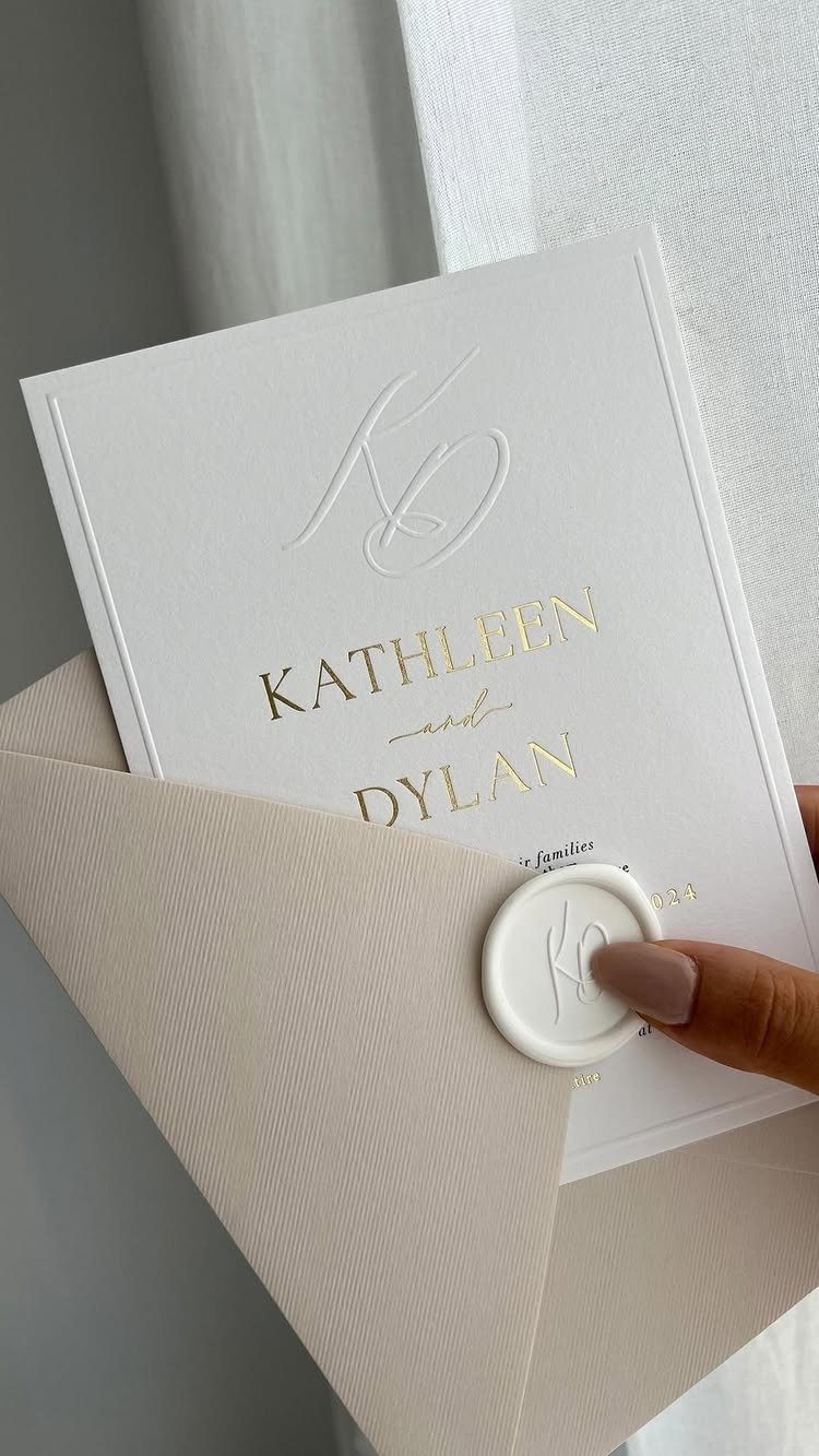 White wedding invitation with gold foil lettering and blind embossed monogram in beige envelope