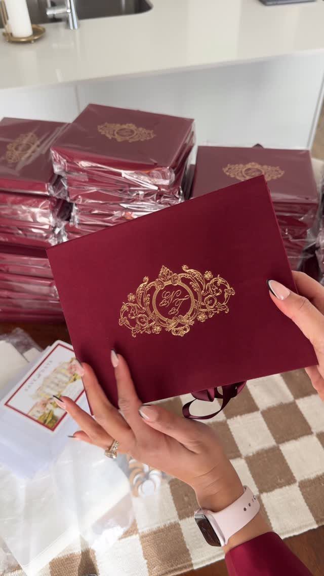 Deep red wedding invitation with gold embossed ornate crest held by a person