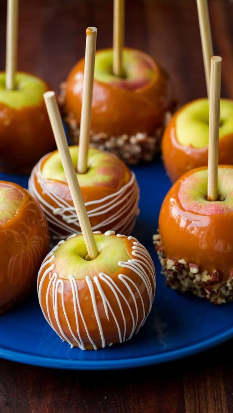 Caramel apples with white chocolate drizzle and nuts on a blue plate.