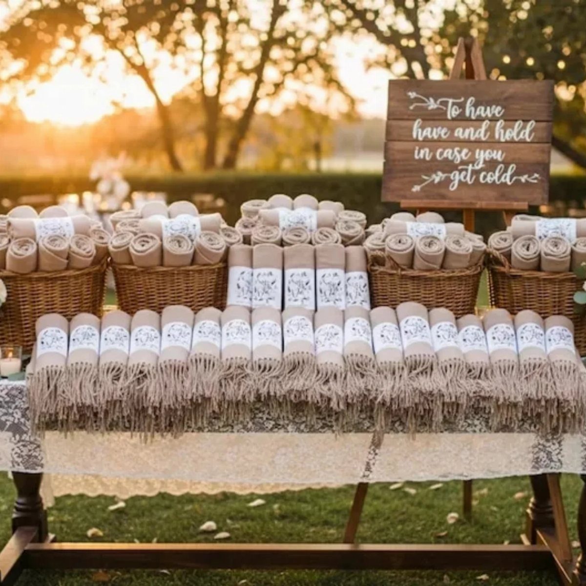 Rolled beige blankets with labels on a lace table at an outdoor wedding.
