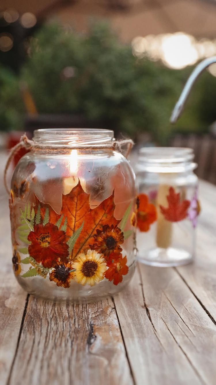 Lit mason jar decorated with pressed autumn leaves and flowers on wooden table
