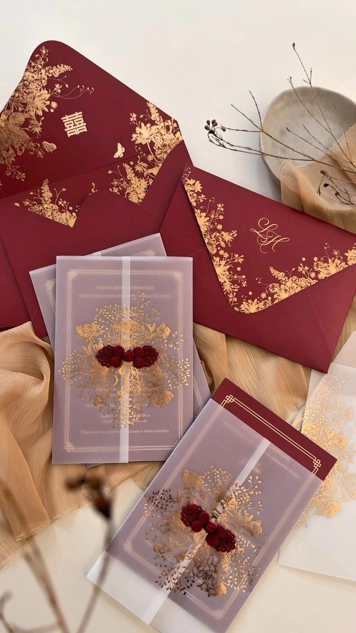 Wedding invitation set with gold foil floral details on red and purple paper.