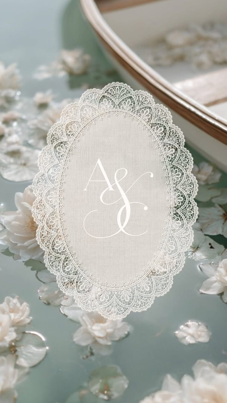 Oval white lace wedding invitation with monogram surrounded by small white flowers