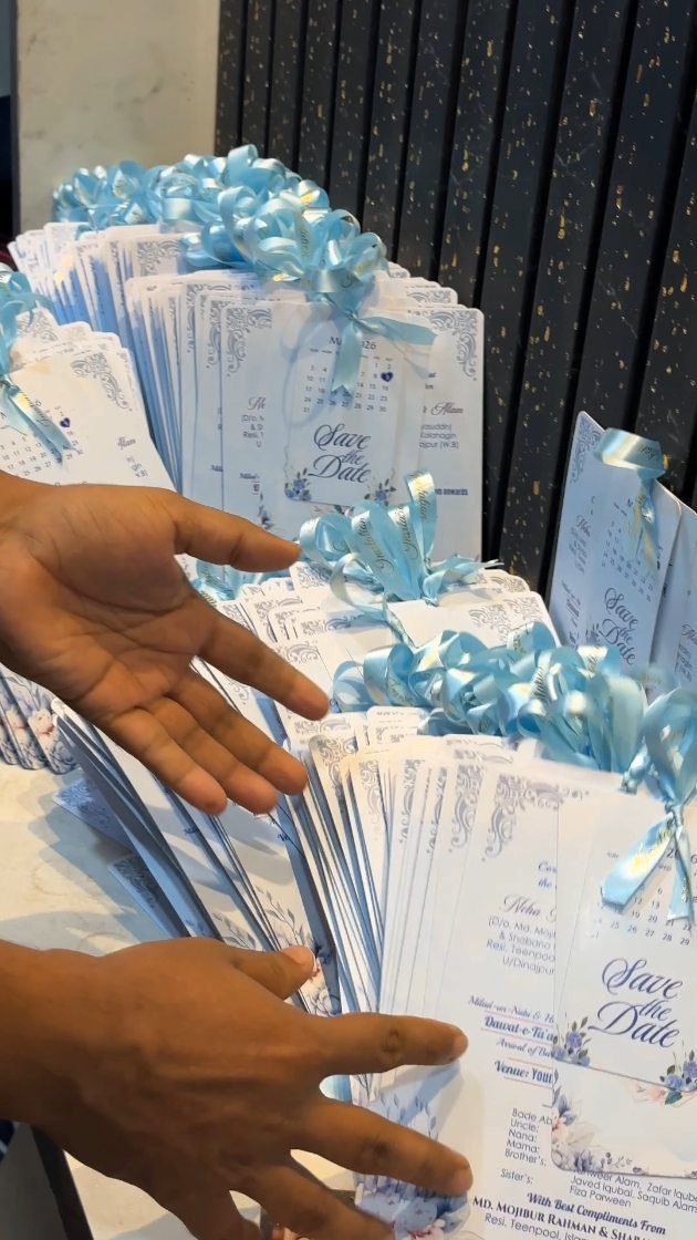 Stacks of white wedding invitations with blue floral accents and light blue ribbons.