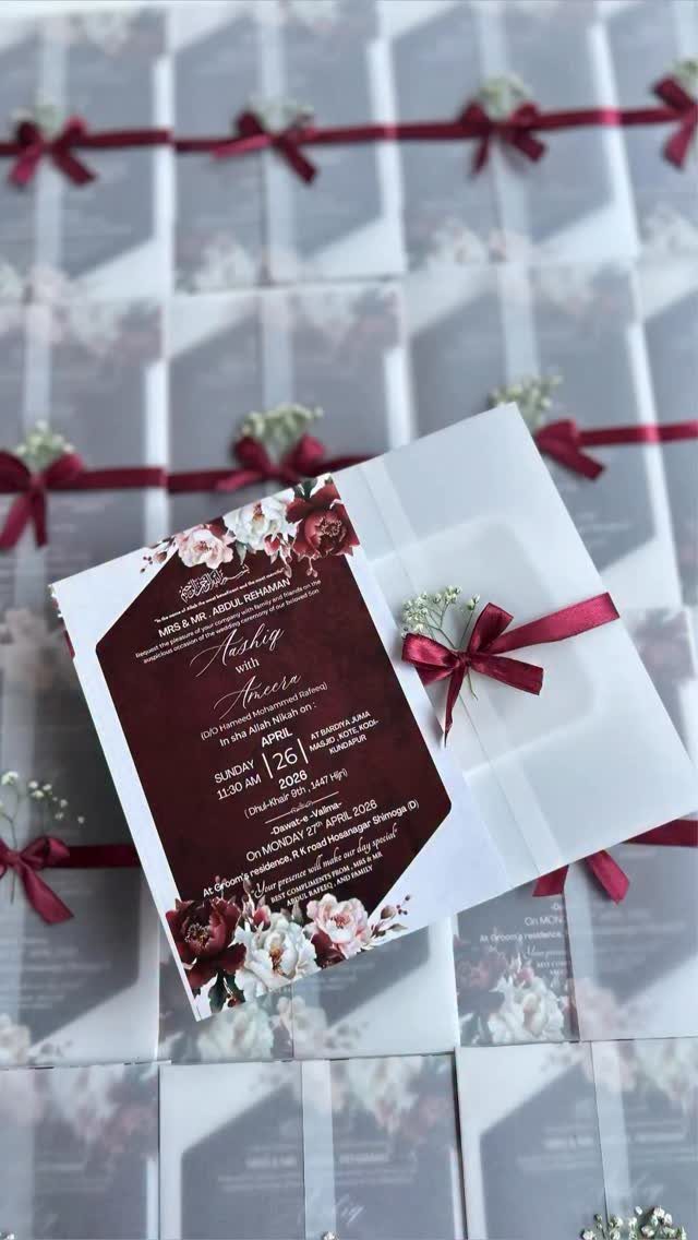 Wedding invitations with red floral designs wrapped in vellum and red ribbons.