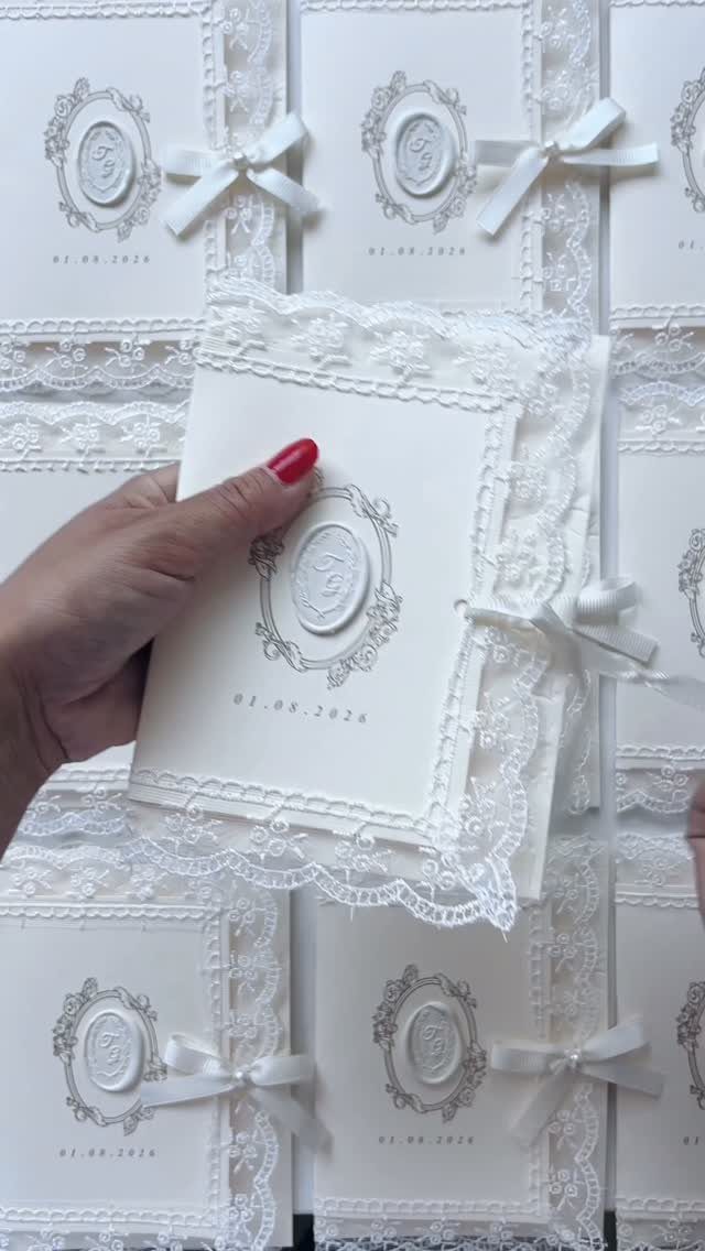 White formal wedding invitation with lace trim, wax seal, and white ribbon bow.