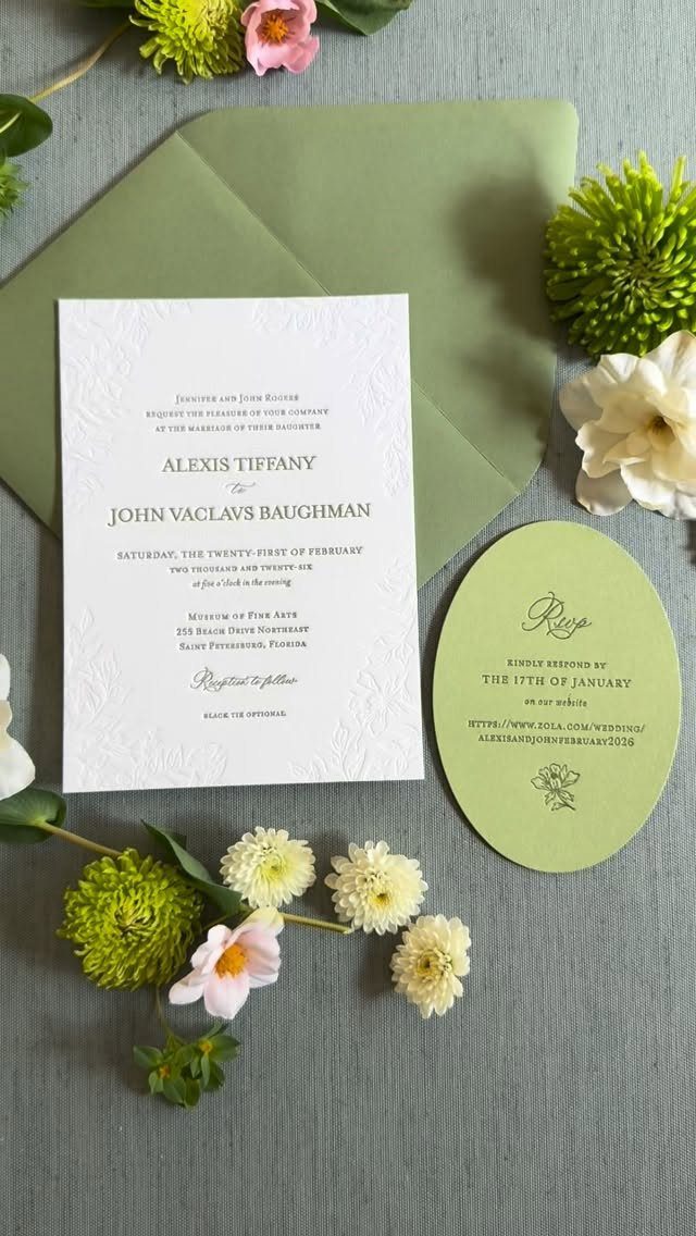 White textured wedding invitation and green RSVP card surrounded by small spring flowers.