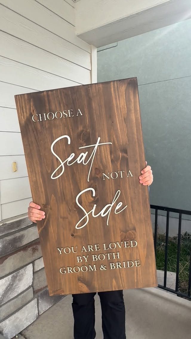 Wooden wedding sign saying Choose a Seat Not a Side held by a person.